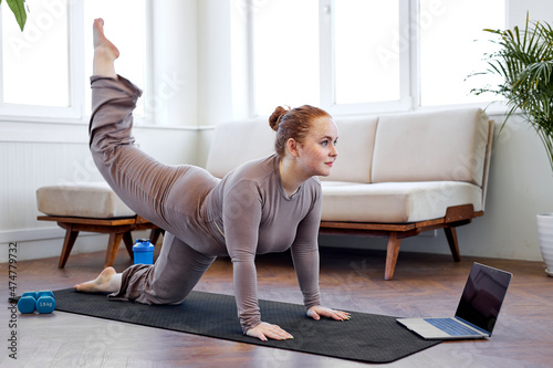 Canvastavla overweight caucasian woman doing sport exercises on fitness mat at home, using laptop