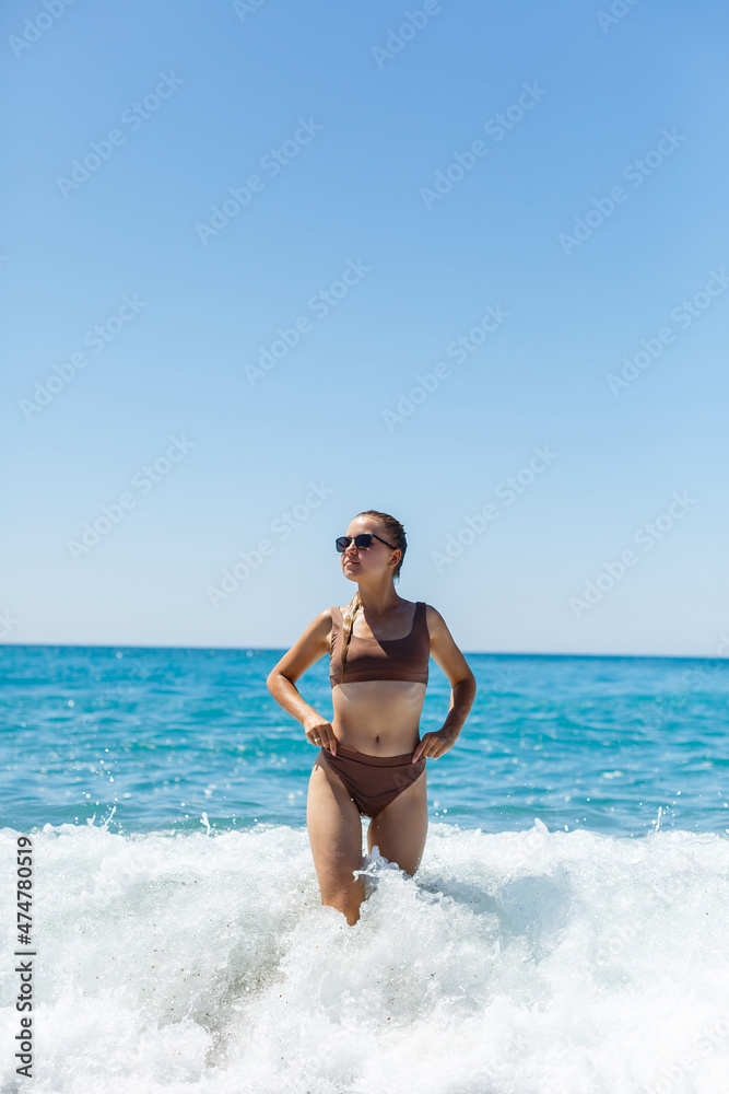 Beautiful woman in a swimsuit and walks on the sand on the beach in Turkey. Holidays in turkey. Photographed with the sea and waves in the background. Selective focus