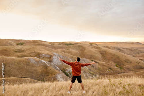 Rear view on sportsman feeling free and excited after sport training, jogging in nature, standing in front of mountains in the morning, wonderful landscape and raising hands up, view from back