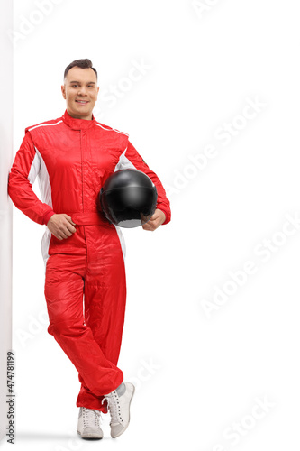 Full length portrait of a racer in a red suit leaning on a wall and holding a black helmet