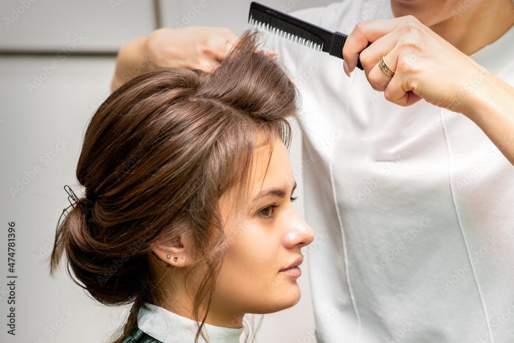 Fototapeta premium Professional hairdresser doing hairstyle for a beautiful brunette young woman with long hair. Concept of fashion and beauty