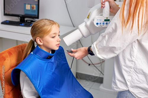 little child girl patient is going to be done panoramic teeth x-ray in dental clinic, side view on caucasian child sitting on dental couch during taking x-ray picture process. health, medicine photo