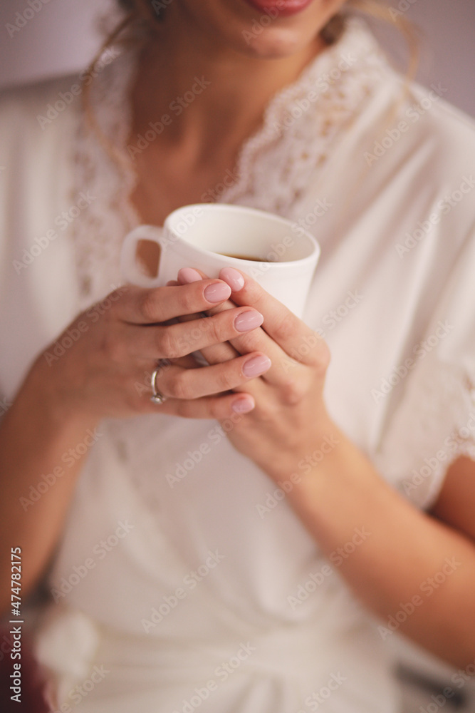 Young woman in white silk robe with white cup of beverage tea or coffee in the morning Young woman in white silk robe with white cup of beverage tea or coffee in the morning