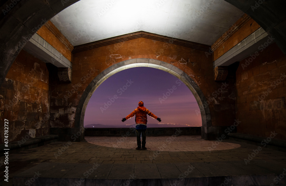 Silhouette of a hiker stands under arch  in the starry night.