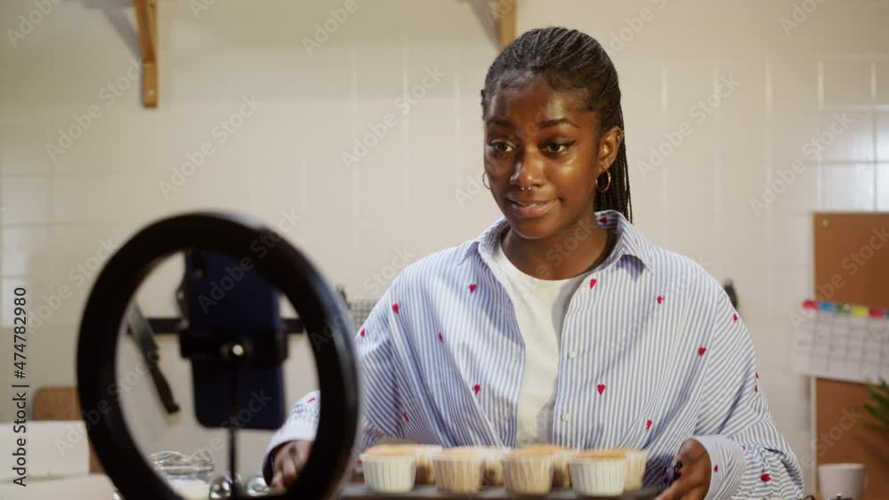 African american chef blogger cooking cupcakes and recording video on smartphone camera. Woman confectioner showing how to prepare muffins, tasty dessert. Baking sweet food, bakery at home. 
