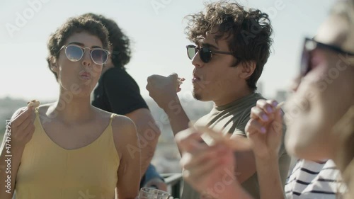 Joyful man and women tasting homemade pizza on rooftop party. Cheerful friends eating savoury fast food, sharing impressions of meal taste, having good time together. Food, leisure activity concept