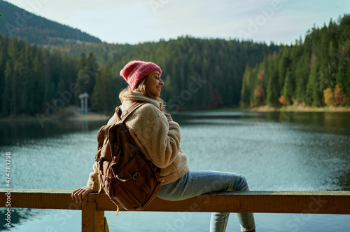 Inspired joyful woman hiker sits on wooden pier at beautiful mountain lake with turquoise water and enjoys her trip into the wild nature location photo