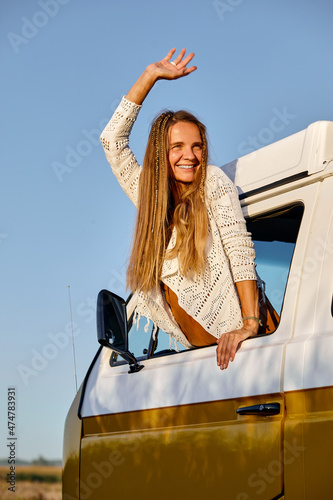 On the way to unknown places. Attractive young woman leaning out the vans window, enjoying the car travel. attractive caucasian female in casual wear, smiling, have rest in nature. travel concept