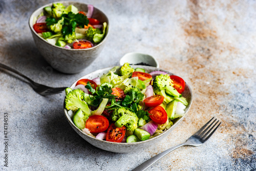 Two bowls of salad with tomato, lettuce, coriander, broccoli, red onion, cucumber and black sesame seeds photo