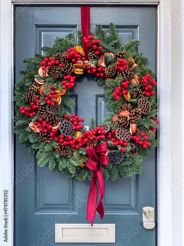 Christmas mood. Elegant christmas wreath decorated red berries, oranges, pine cones and lotus on a grey blue wooden door