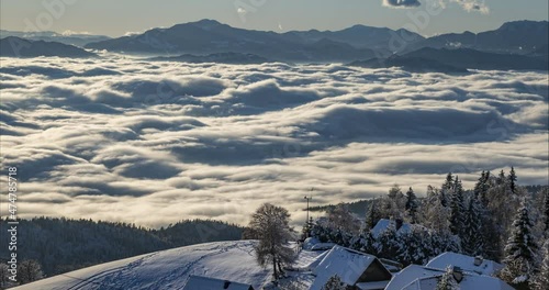 Time lapse of inversion clouds moving in alpine valley. Beautiful landscape in winter season. Small village in the mountains in Slovenia. Low moving fog with long shadows. Aerial or elevated view