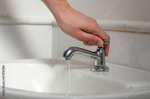 a white male hand turning off a sink faucet
