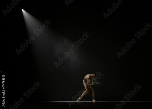 Male performer under a stage light holding his head in his hands in despair photo