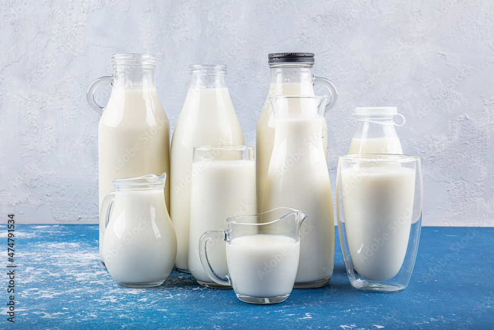 Pure milk drinks in clear jars and bottles are naturally healthy foods placed on a blue background. A bottle of milk and glass of milk on a wooden table on a blue background. Pure milk drinks in clear jars and bottles are naturally healthy foods placed on a blue background. A bottle of milk and glass of milk on a wooden table on a blue background.