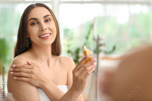 Young beautiful woman with bottle of essential oil in bathroom photo