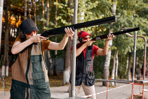 Focused caucasian skilled people in goggles and headset on tactical gun training classes, aiming rifle at target. Shooting and Weapons. Outdoor Shooting Range At Summer Evening. Side View.