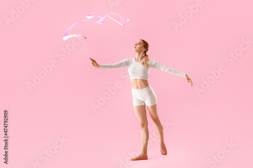 Beautiful young woman doing gymnastics with ribbon on color background