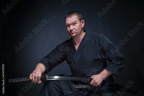 A man in a samurai kimono holding a katana in his hands on a black background, studio session photo