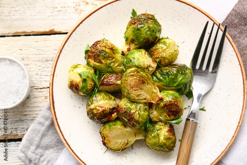 Plate with tasty roasted Brussels cabbage and sea salt on light wooden background