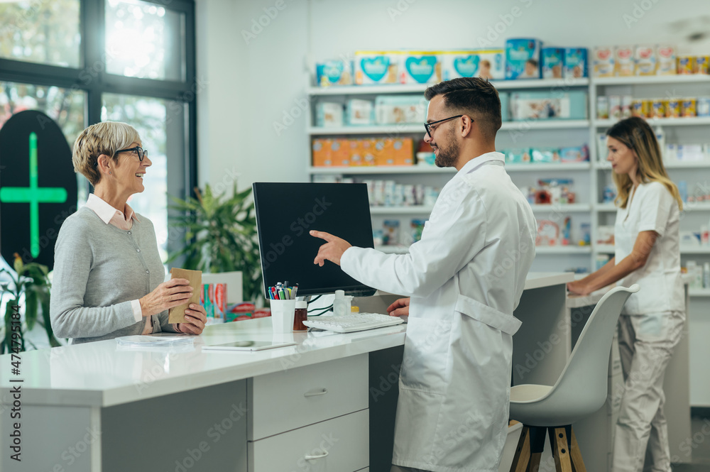 Young male pharmacist giving prescription medications to senior female customer in a pharmacy Young male pharmacist giving prescription medications to senior female customer in a pharmacy