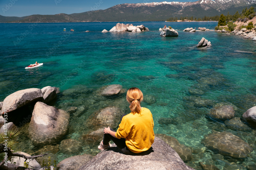 Young woman in yellow shirt enjoying the view of Emerald Bay at Lake Tahoe, California, USA. The largest alpine lake in North America Lake Tahoe