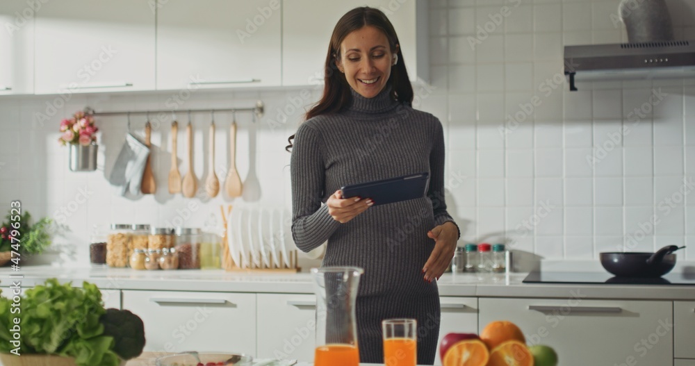 pregnant using digital tablet in kitchen at home