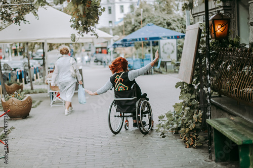 girl in wheelchair rides with hands to side through old town on sidewalk near cars. Freedom of movement of persons with special needs