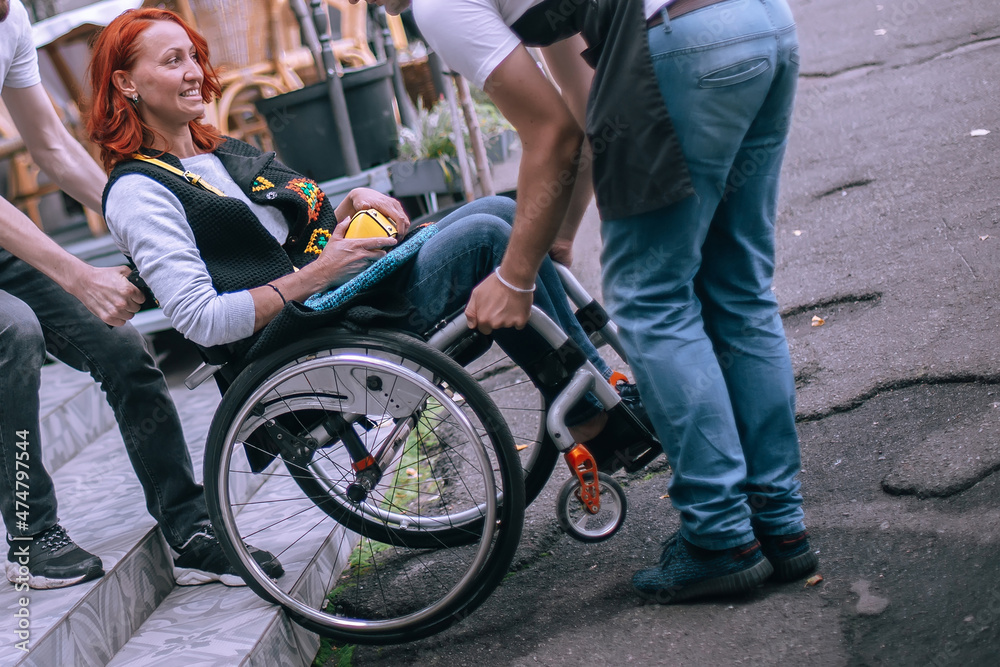 Obraz premium Waiters lift a girl in a wheelchair up the steps without a ramp. A woman is going to have lunch in a cafe inaccessible to people with special needs