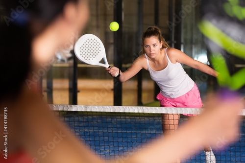 Portrait of sporty young brown-haired girl playing padel on indoor court, ready to hit ball. Healthy and active lifestyle concept. © JackF