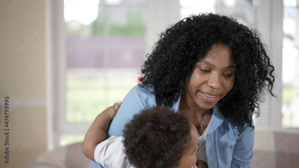 Young woman dancing with toddler boy in hands in living room at home. Happy satisfied African American mother enjoying leisure with son indoors on weekend. Family lifestyle concept Young woman dancing with toddler boy in hands in living room at home. Happy satisfied African American mother enjoying leisure with son indoors on weekend. Family lifestyle concept