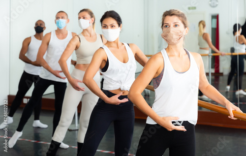 Group of men and women in protective masks practicing at the ballet barre