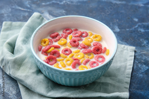 Bowl of colorful cereal rings and milk on color background