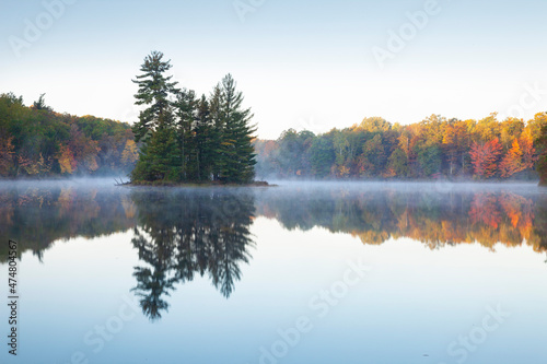 Beautiful calm lake with trees in autumn color and a small island in northern Minnesota at dawn