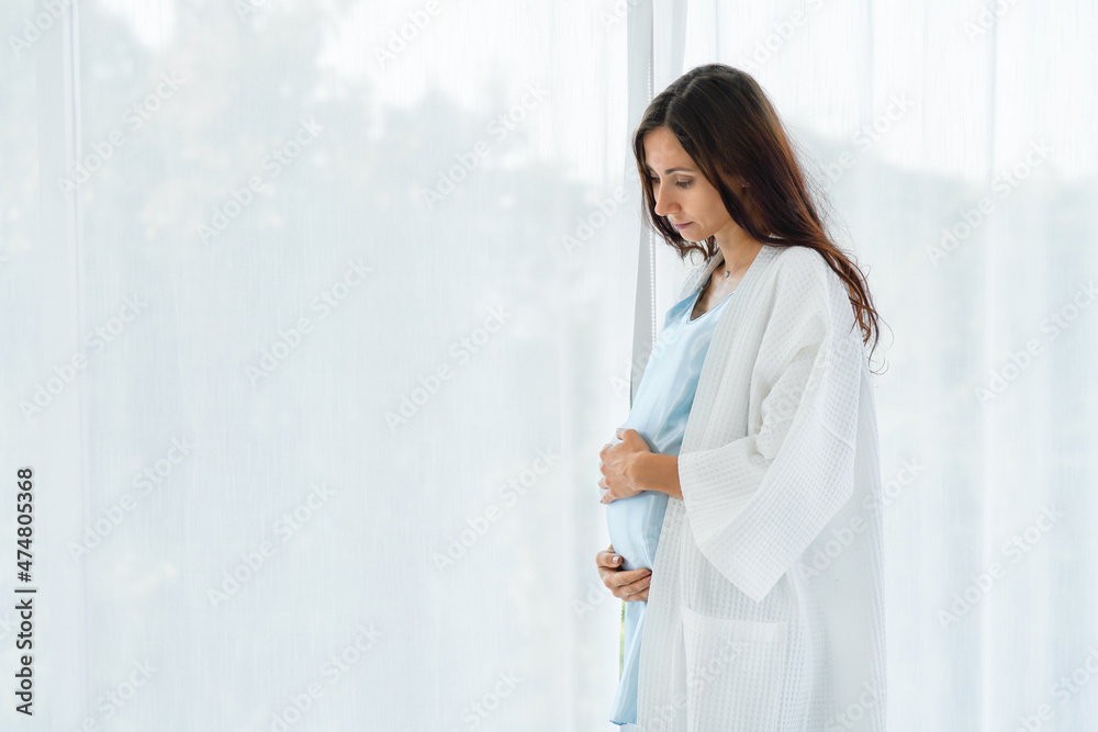 pregnant woman standing at home with hands touching stomach pregnant woman standing at home with hands touching stomach