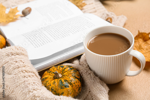 Cup of tasty coffee  book and autumn decor on beige background