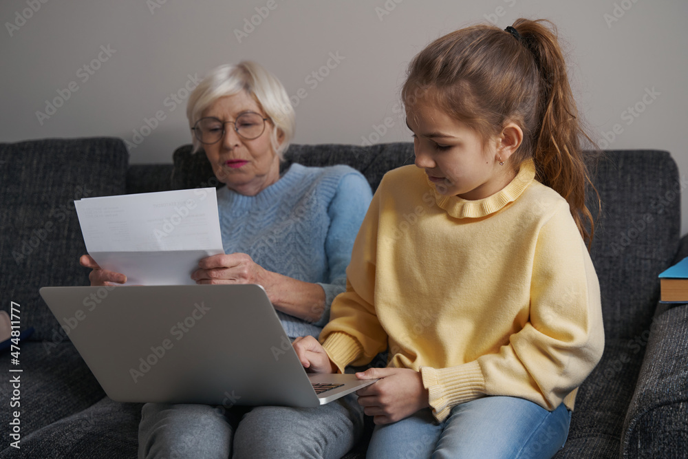 Talented young child working on laptop near her grandma