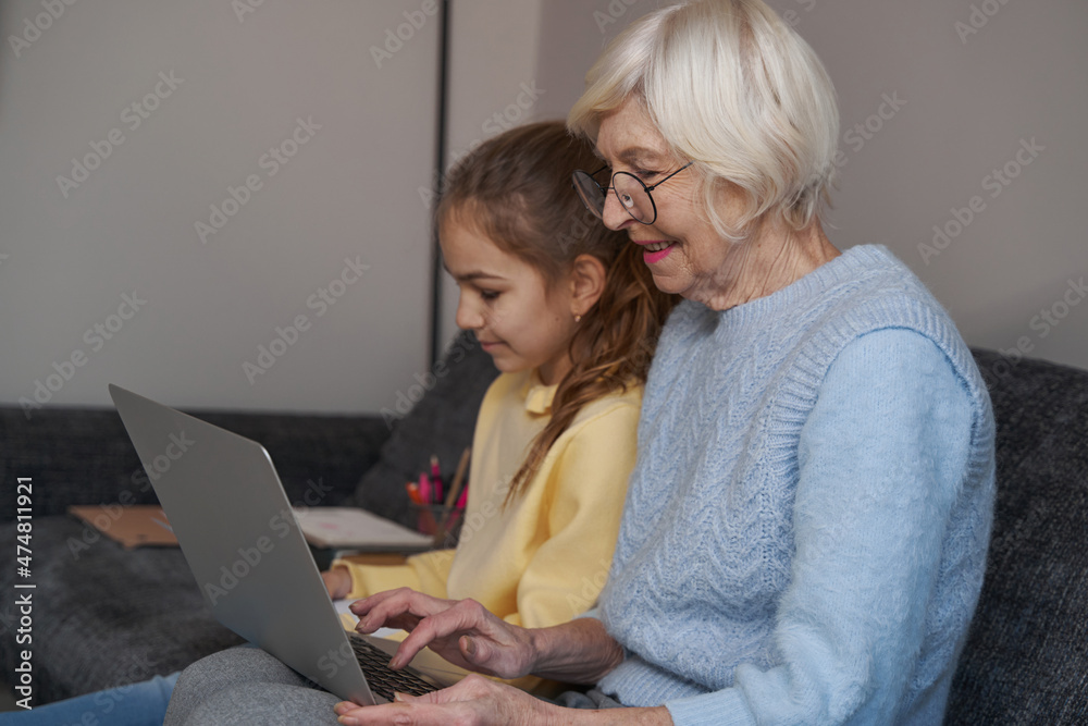 Merry grandma using laptop while spending time with granddaughter Merry grandma using laptop while spending time with granddaughter