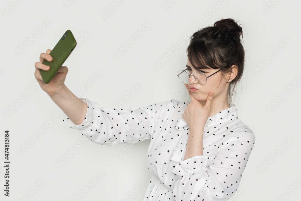 Side view of a student making a duck face and taking a self portrait with her smart phone.