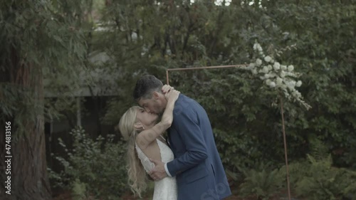 A married wedding couple embracing, hugging, and kissing in an wooded outdoor area.