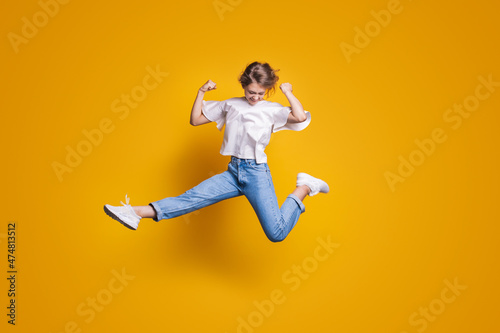 Photos Woman in casual jeans clothes jumping with raised hands and legs isolated on yellow background
