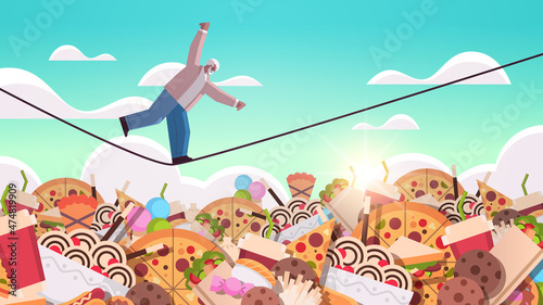 senior man balancing on rope above junk food assortment of fast food unhealthy nutrition junkfood addiction concept
