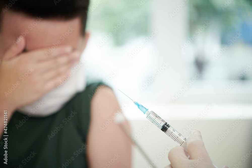 Scared boy covering eyes with hand when doctor showing syringe with vaccine against coronavirus Scared boy covering eyes with hand when doctor showing syringe with vaccine against coronavirus