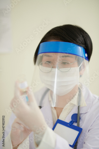 Female doctor in protective face shield and medical mask filling suringe with vaccine