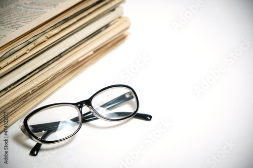 Stack of old newspapers and reading glasses on a white background.