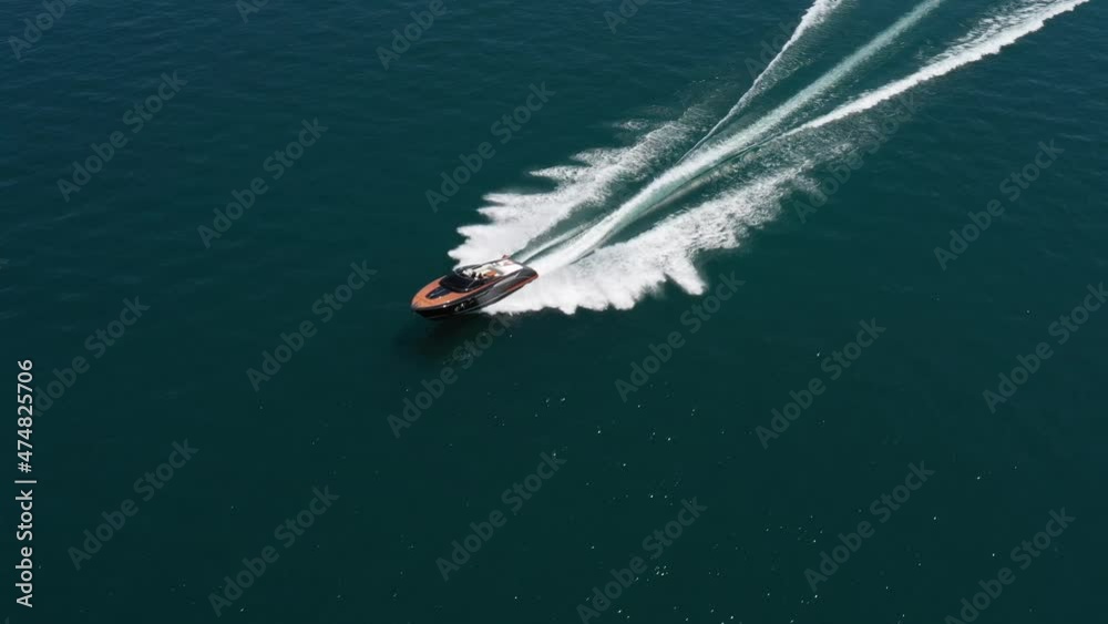 Luxury boat in dark color, fast movement on blue water, aerial view. Expensive luxury Italian boat moving on the water top view. Boat dark wood, movement on the water top view.