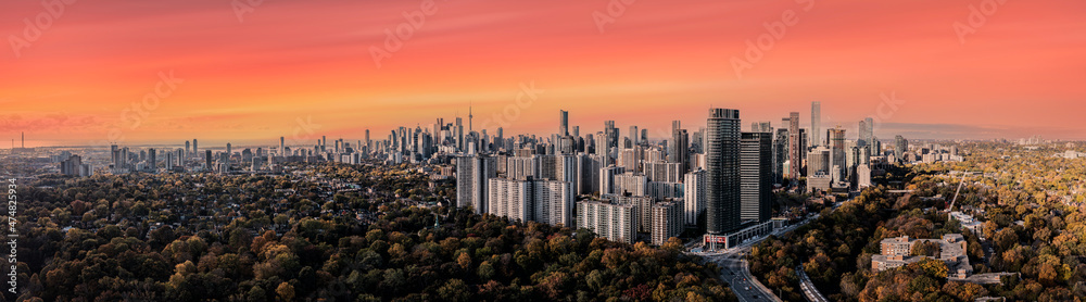 Toronto skyline with city buildings and cntower in view in the fall with yellow trees and red skies 