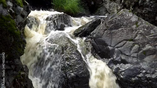 Small waterfall among trees and rocky cliffs in National Park in Southern Russia. Mountain waterfall beats in small streams around huge stones covered with moss