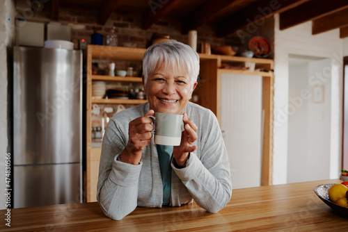 Tableau sur toile Portrait of retired biracial elderly female leaning on kitchen counter smiling at camera