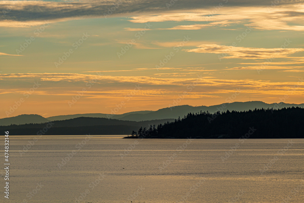 sunset by the coast at golden hour with cloud filled orange sky above the islands on the ocean