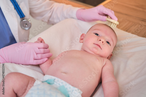 The doctor is combing the hair of a newborn baby. Nurse in uniform with a comb in hand for a child